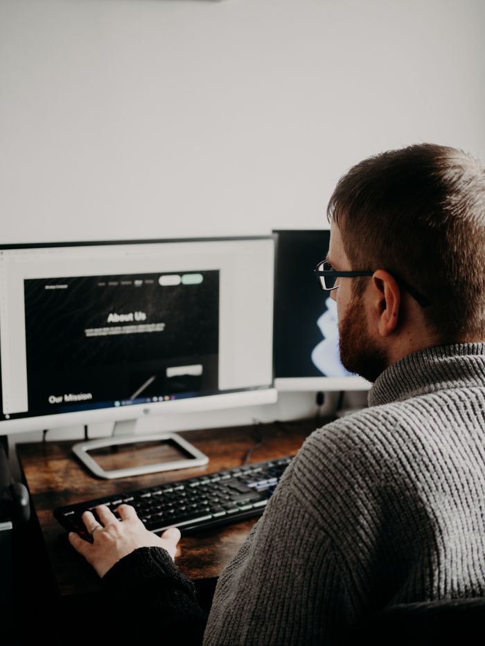 creative-01 Man working on web design at home office setup with dual monitors.